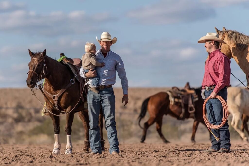 Family and ranch hands smiling by a barn door